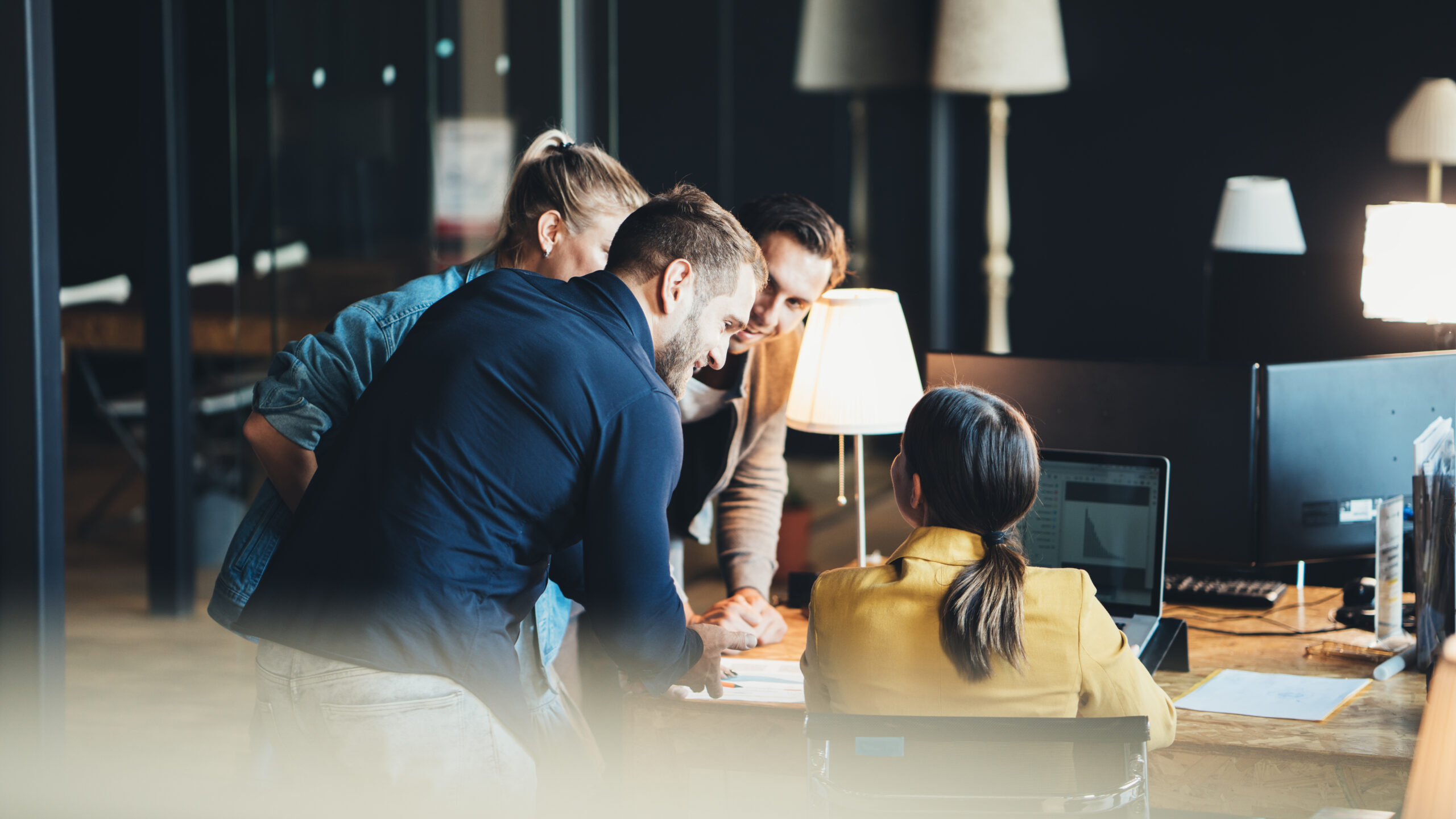 Team collaborating in a modern office around a computer, discussing financial transformation and Sage Intacct solutions.